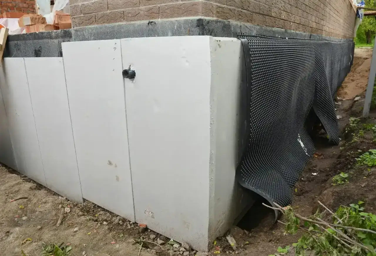 Płyty izolacyjne i membrana kubełkowa to skuteczne sposoby, czym zabezpieczyć fundamenty przed wilgocią.