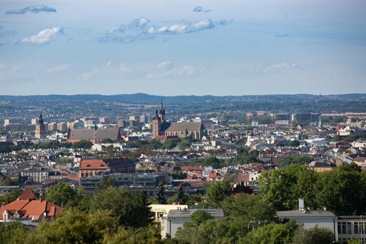 Panorama Krakowa z dominującymi kościołami i zielenią. Widać wiele dach&oacute;w i budynk&oacute;w, tworząc obraz pięknych miejsc w Krakowie.