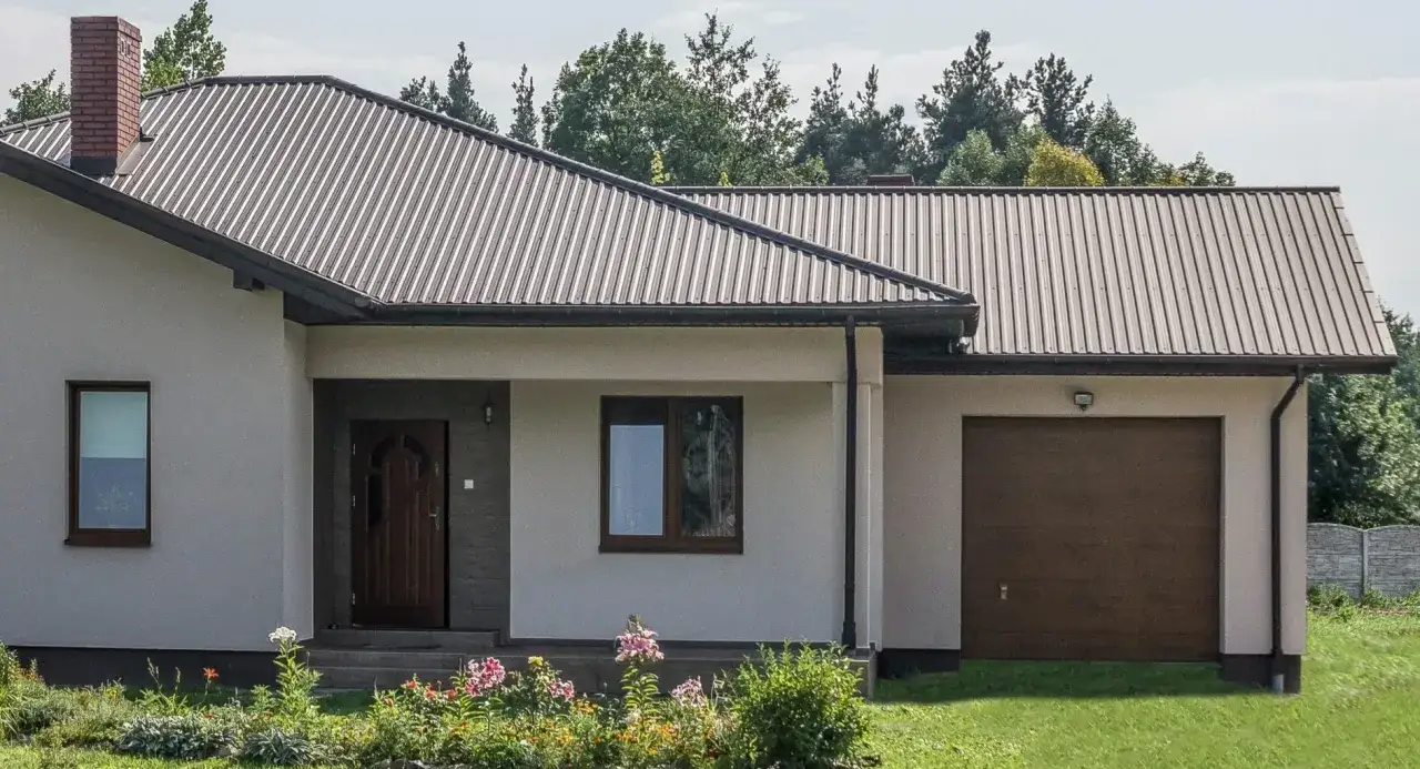 Nowy dom z dachem z blachy trapezowej. Wymiary dachu dopasowane do bryły budynku, z widocznym kominem i garażem.