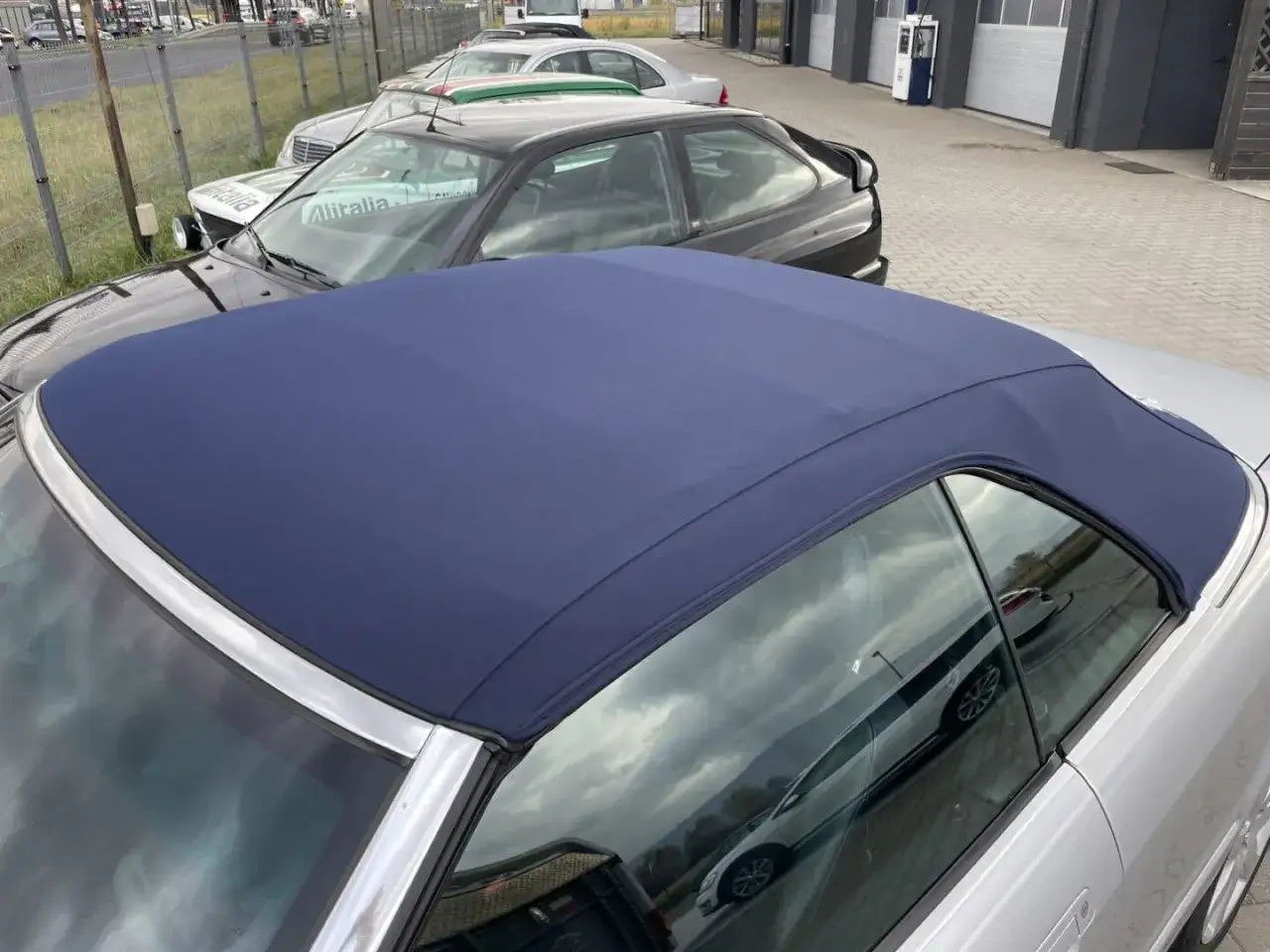 Nowy, granatowy szycie dachu cabrio na srebrnym samochodzie. W tle inne auta i budynki.