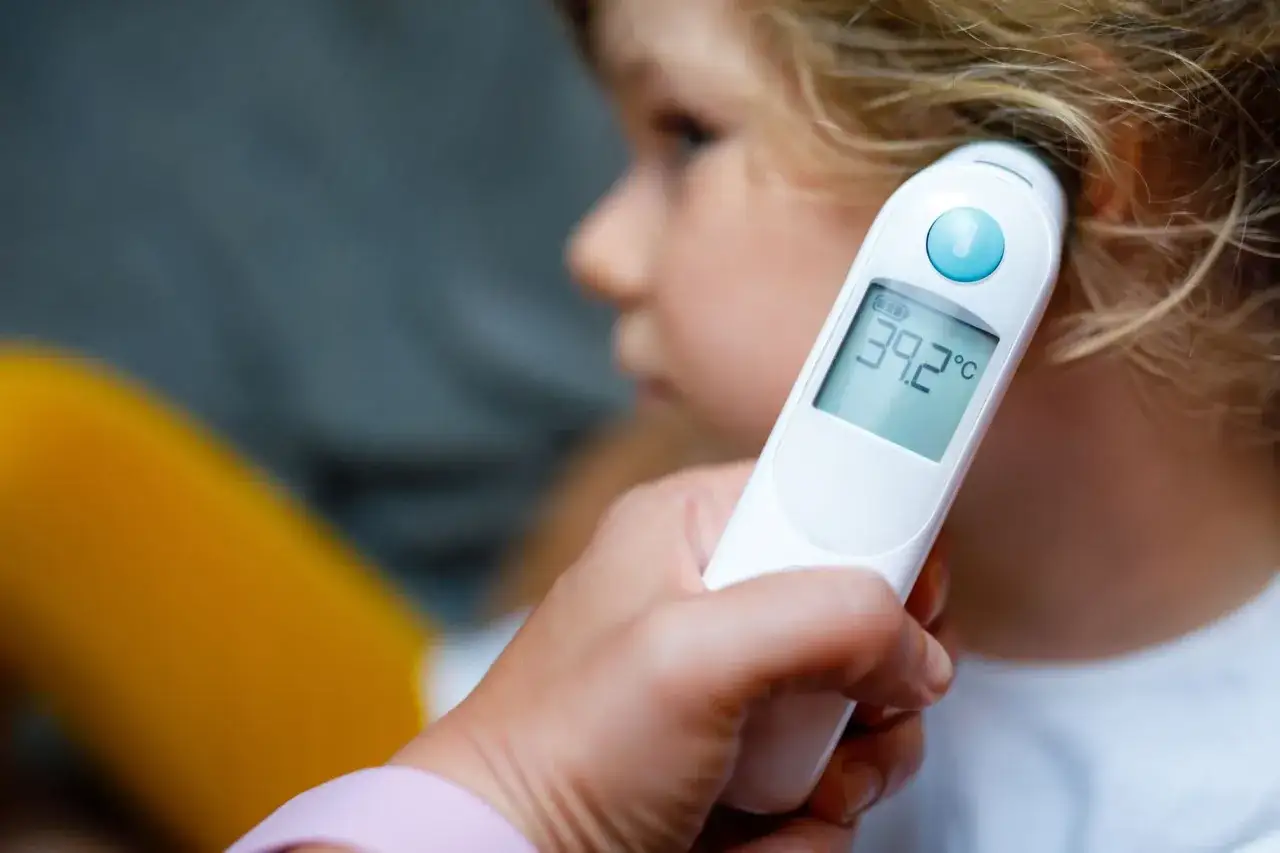 Gorączka 39.2&deg;C u dziecka. Zbliżenie na termometr elektroniczny przykładany do ucha malucha.