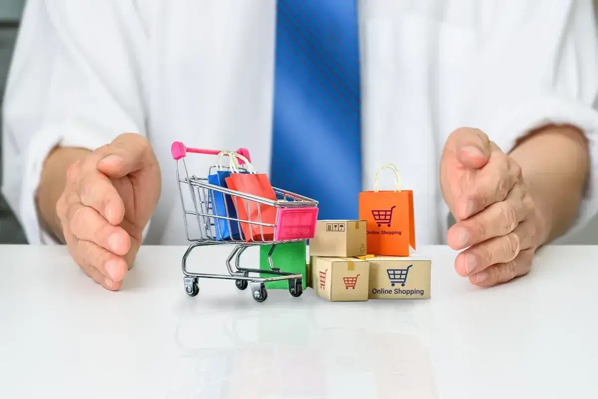 Rękojmia a gwarancja w e-commerce: wózek z zakupami i paczki pod ochroną dłoni.