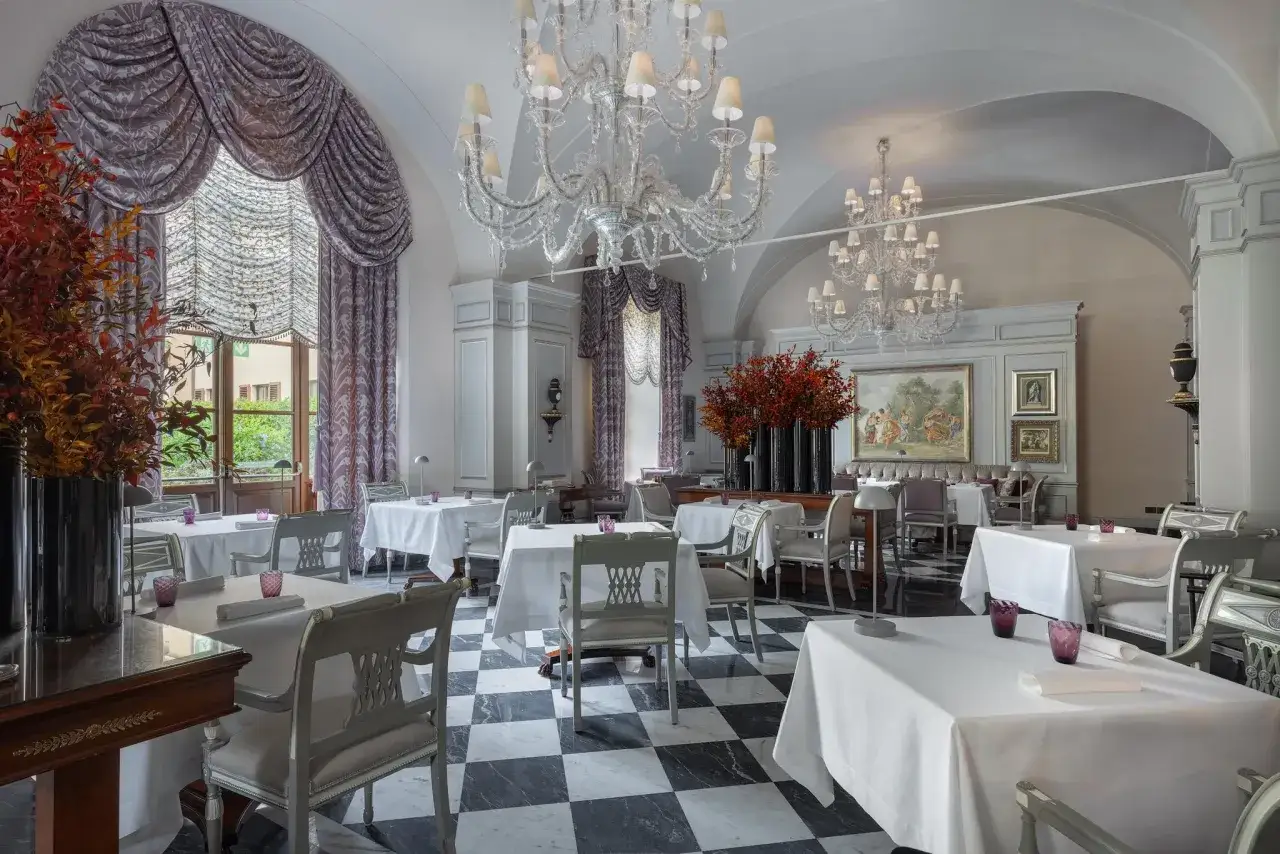 Elegante sala da pranzo con tavoli apparecchiati, lampadari di cristallo e un quadro che ricorda un atto di Vito Mollica.