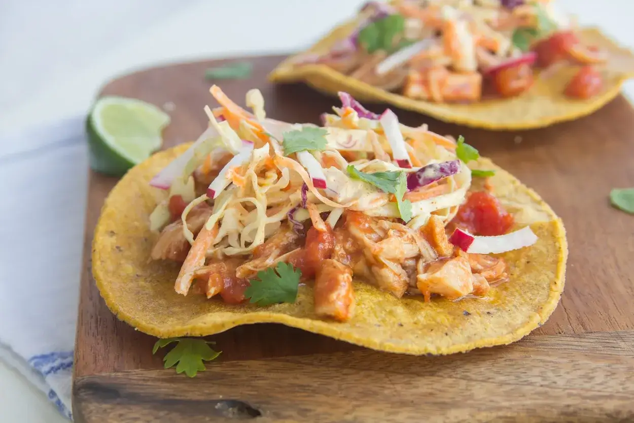 Två läckra tostadas med kyckling tinga, toppade med krispig kålsallad och färsk koriander. En limeklyfta ligger bredvid.