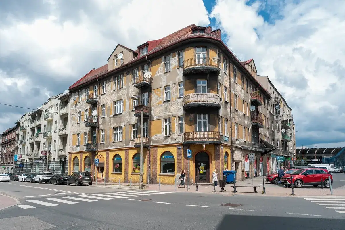 Kamienice w trakcie remontów, z żółtą elewacją i balkonami, czekają na odnowienie.