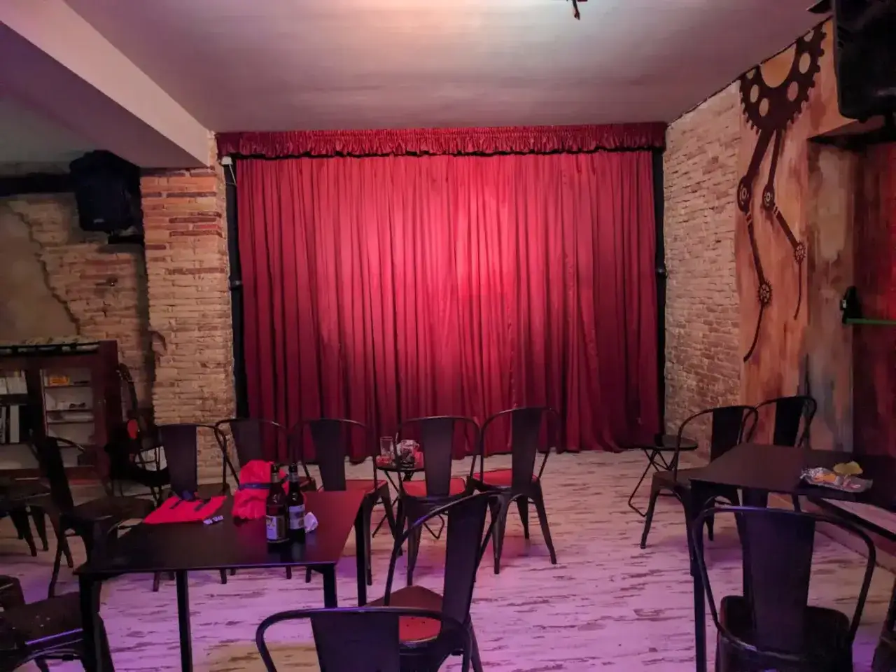 El escenario de el.sotano magico espera. Cortinas rojas, sillas metálicas y un ambiente íntimo para una noche de espectáculo.