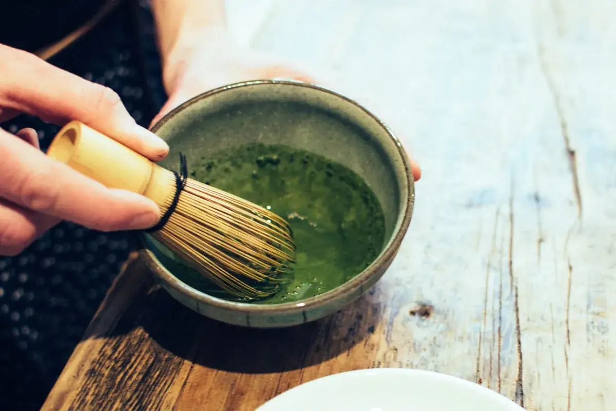 En hand vispar intensivt grönt matcha innehåll i en skål med en bambuvisp.