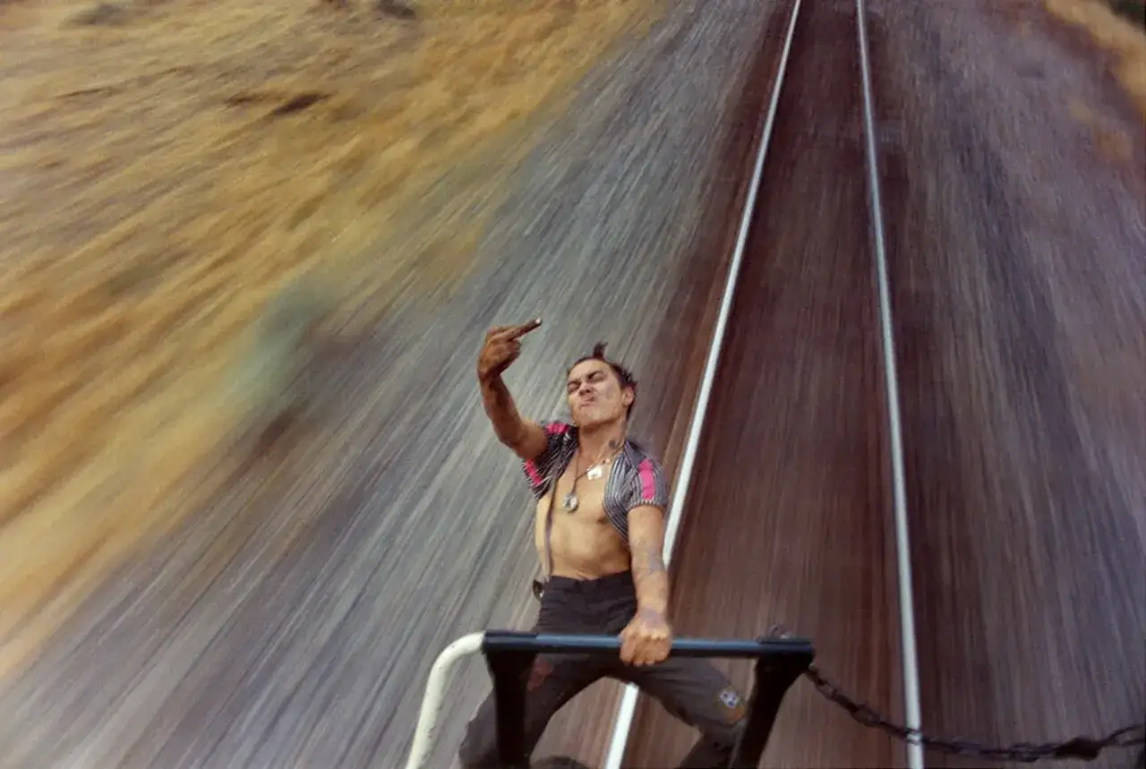 A defiant figure on a train, captured by mike brodie photography, flips the bird against a blur of motion.