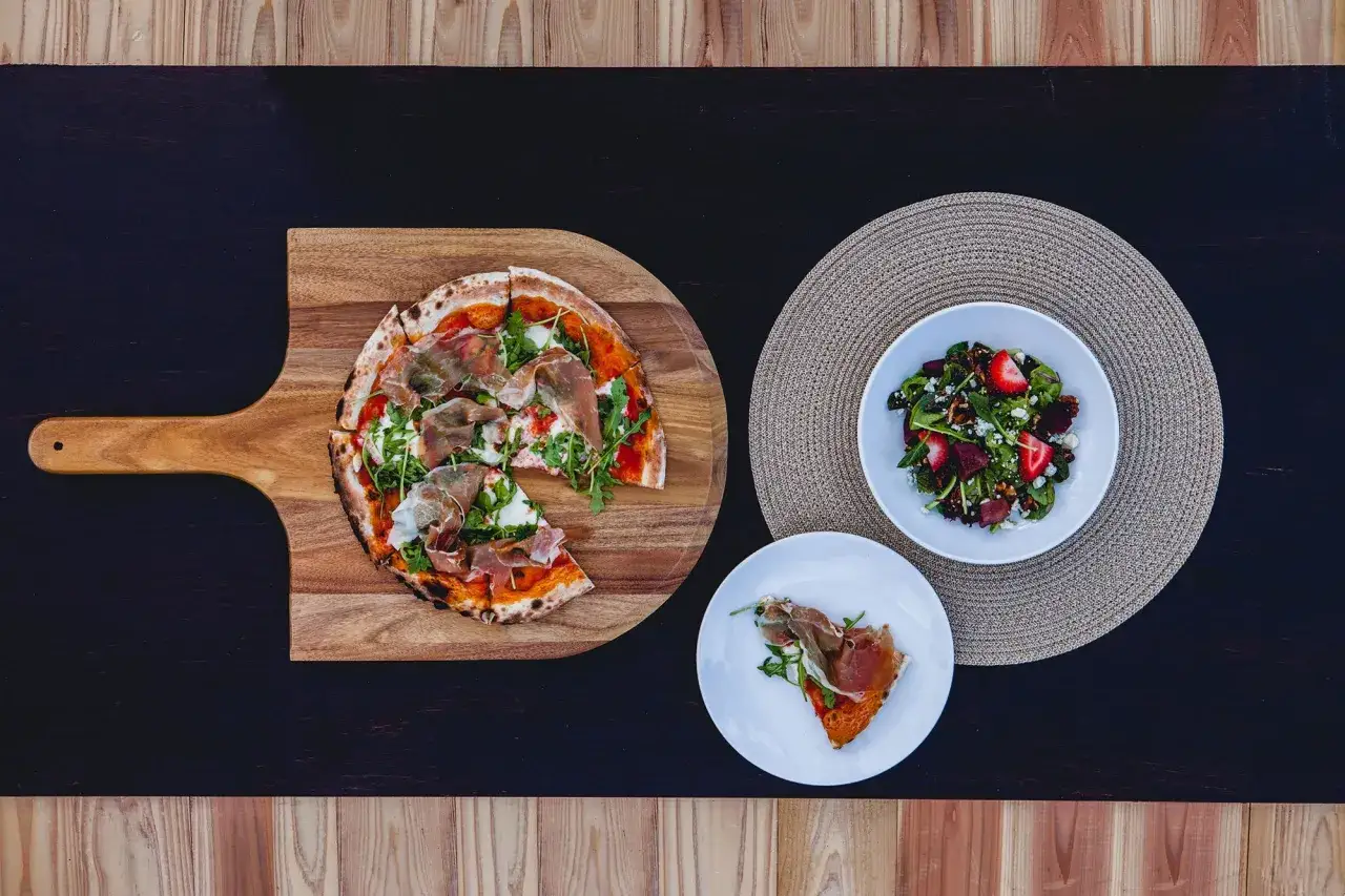Idealny posiłek, gdy jest światowy dzień pizzy: pizza z rukolą i szynką parmeńską, sałatka z truskawkami i serem pleśniowym.
