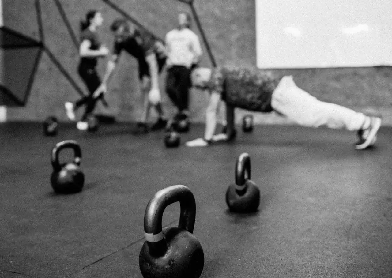 Ćwiczenia z kettlebellami na siłowni. Grupa os&oacute;b w tle, jeden mężczyzna w pozycji deski. Idealne dla kurs pielęgniarski dla początkujących.