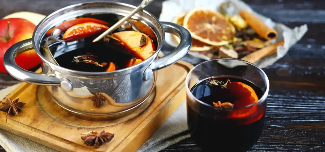 Aromaticzny grzaniec galicyjski w garnuszku i szklance, z dodatkiem jabłek, pomarańczy i przypraw.