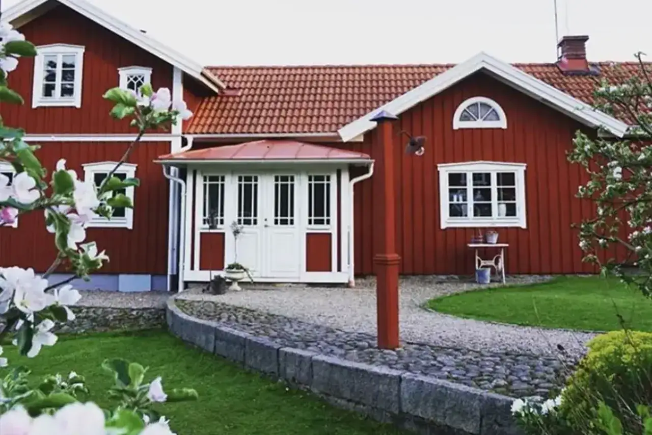 Ett r&ouml;tt tr&auml;hus med vita f&ouml;nster och d&ouml;rrar, en vacker tr&auml;dg&aring;rd och en stenlagd g&aring;ng. Planer p&aring; att bygga ut det gamla huset f&ouml;r mer utrymme.
