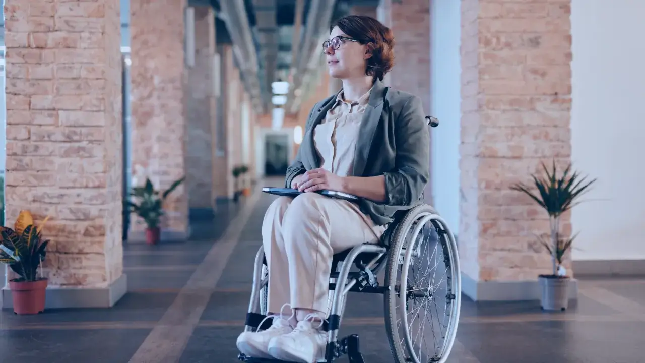 Kobieta na wózku inwalidzkim z laptopem na kolanach, zastanawia się, czy osoba niepełnosprawna może pracować w soboty i niedzielę.