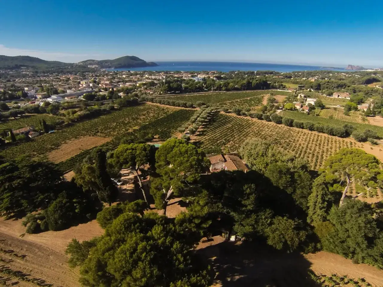Vue aérienne du **Château Pradeaux** et ses vignobles s'étendant vers la mer Méditerranée, sous un ciel bleu éclatant.