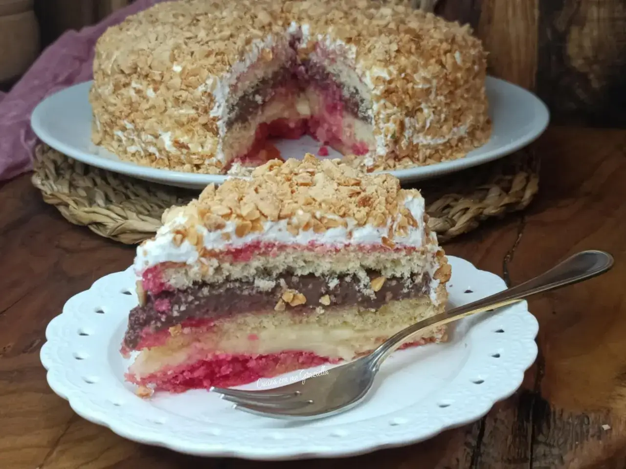 Fetta di zuppa inglese con strati di pan di spagna, crema pasticcera, cioccolato e fragole, ricoperta di panna e granella di nocciole.