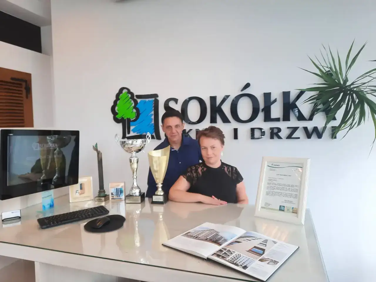 Para z trofeami przed logo firmy