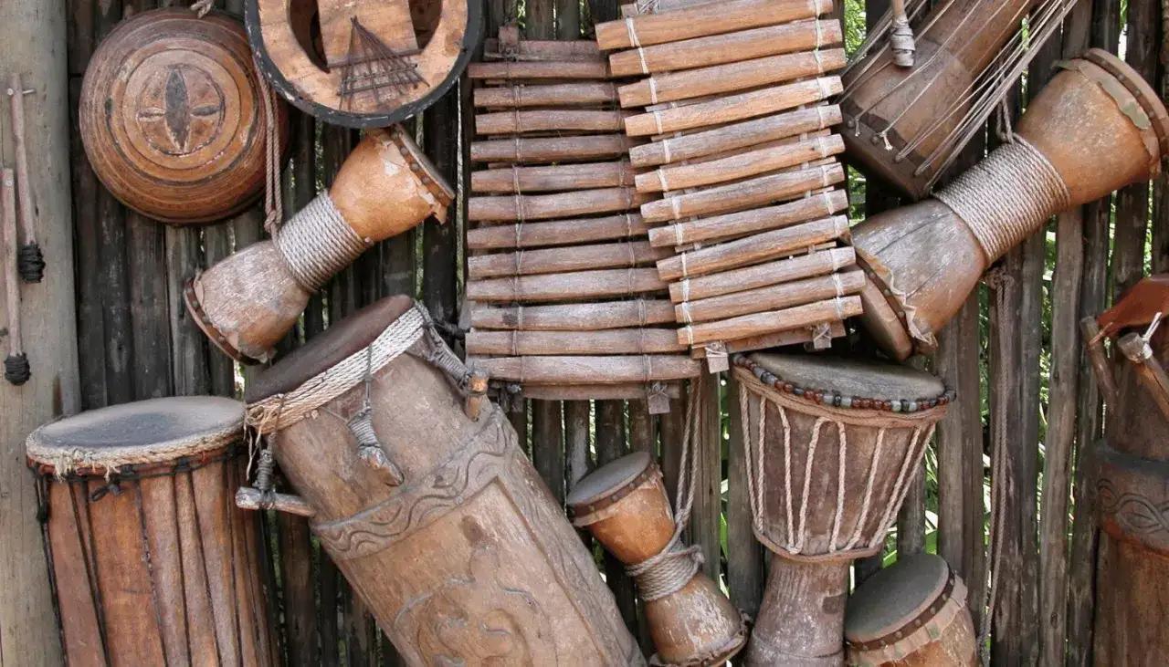 Collection de divers types de tambours africains en bois, certains d&eacute;cor&eacute;s, suspendus &agrave; une palissade.