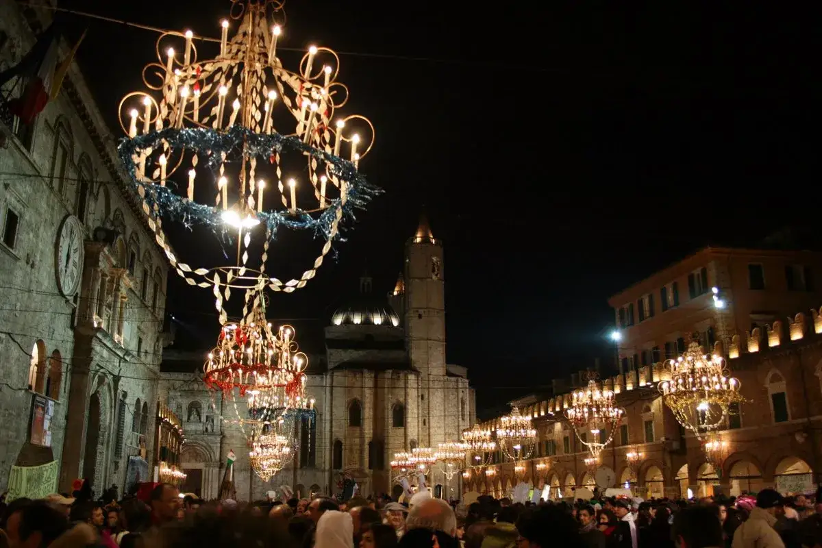 Luci scintillanti e grandi lampadari illuminano la piazza per il carnevale di Ascoli. Una folla festante ammira le decorazioni.