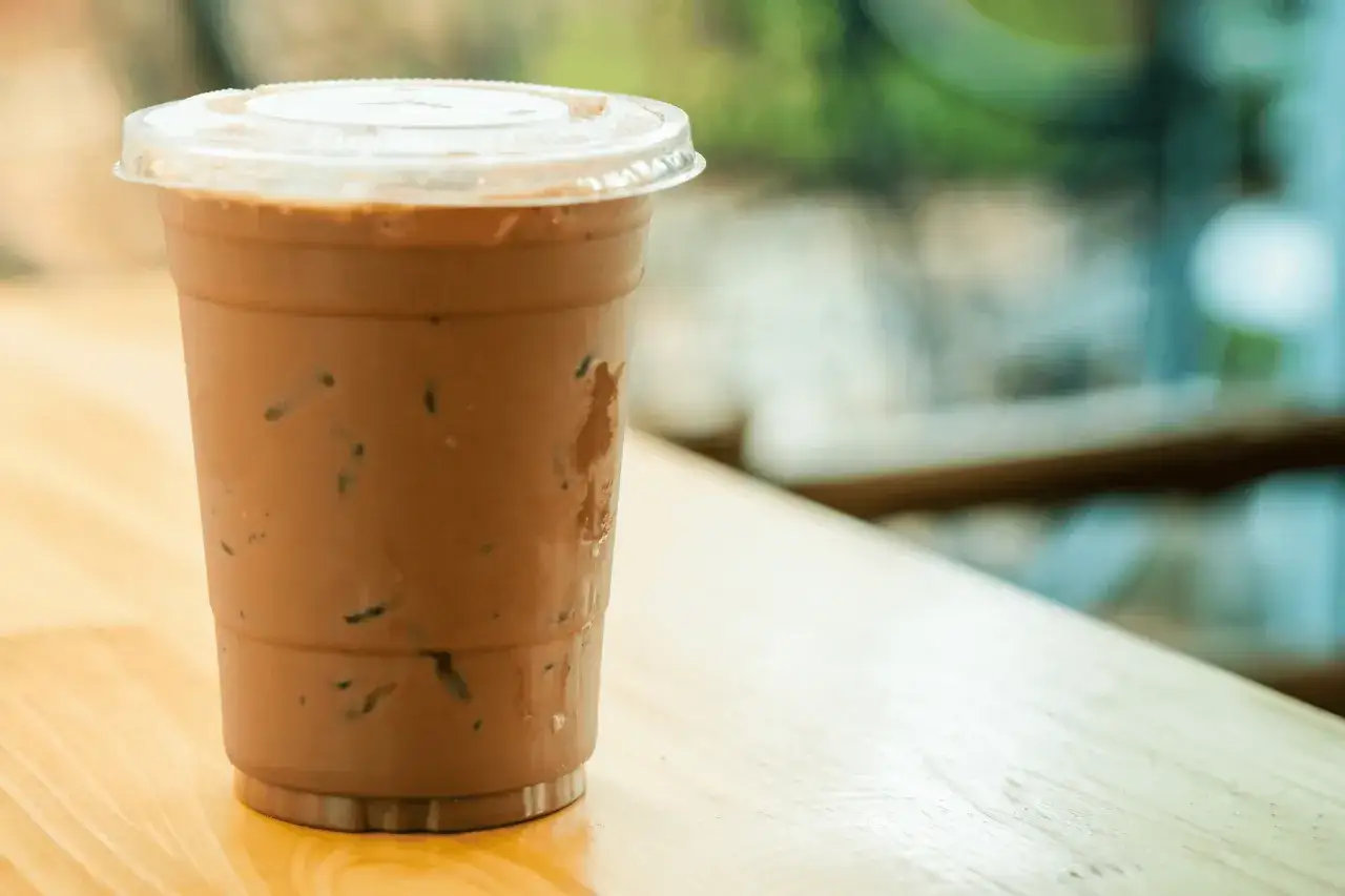 Un bicchiere di caff&egrave; decaffeinato freddo, perfetto per i bambini, con ghiaccio e una cannuccia, su un tavolo di legno.