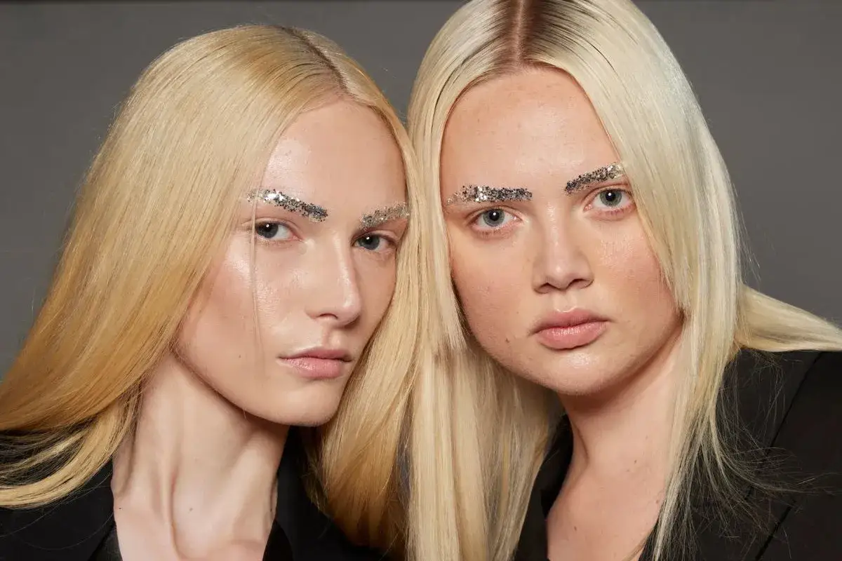 Dwie modelki o blond, niemal ż&oacute;łte włosy, z brokatem na brwiach.