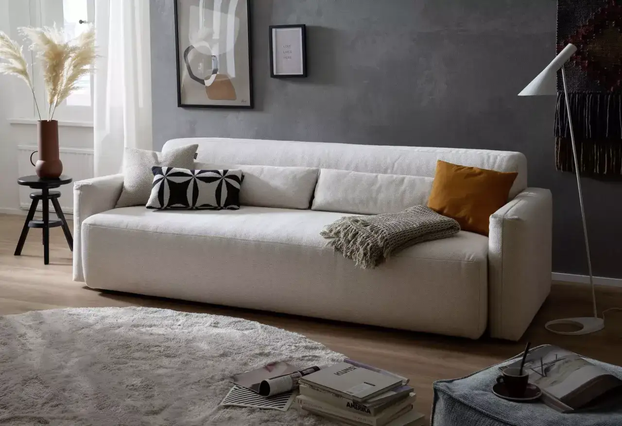 Ein helles Schlafsofa mit Kissen und Decke, ein typisches Merkmal eines Schlafsofas für gemütliche Abende.