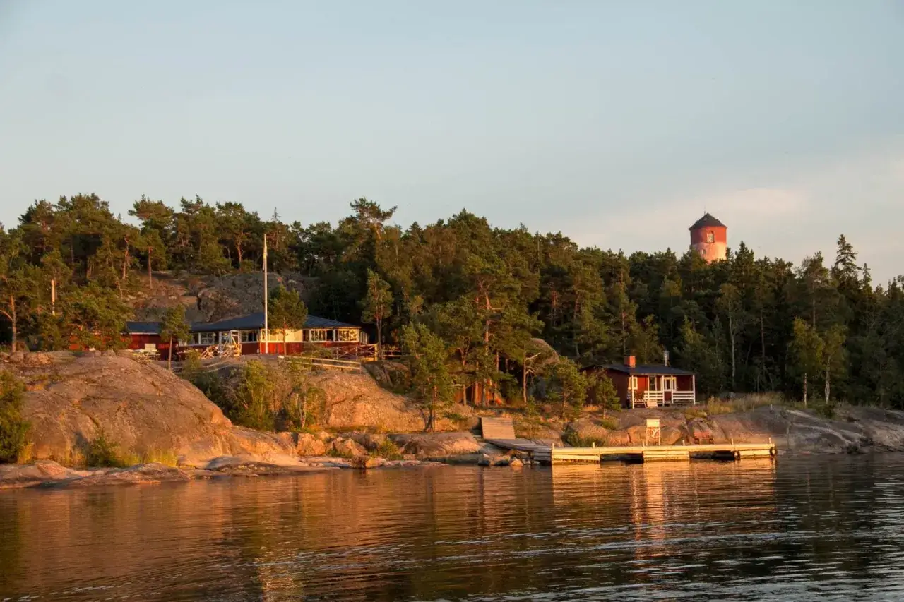 R&ouml;da hus och en fyr p&aring; en klippig &ouml; med tallskog. Vackert arholma boende vid vattnet i solnedg&aring;ngen.