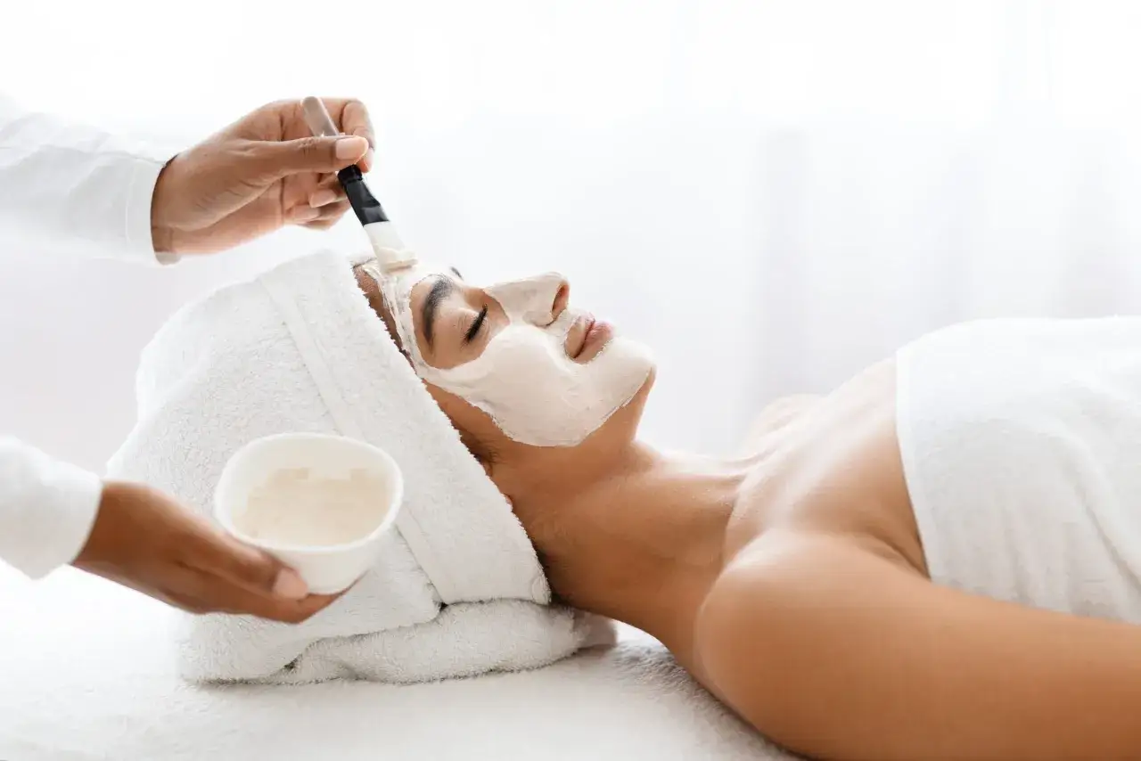 Une esth&eacute;ticienne applique un masque apaisant sur le visage d'une femme lors d'un soin de nettoyage de peau.