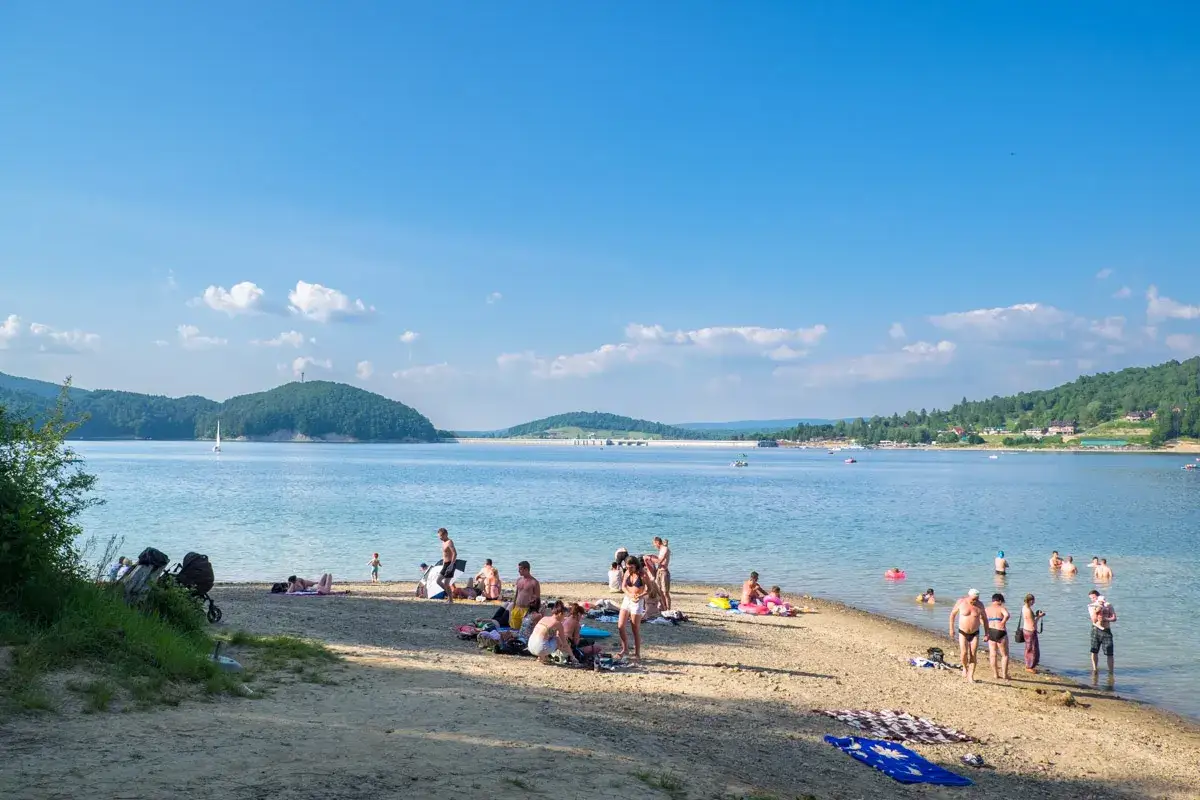Polańczyk atrakcje: plażowicze odpoczywają nad Soliną, w tle żaglówka i zielone wzgórza.