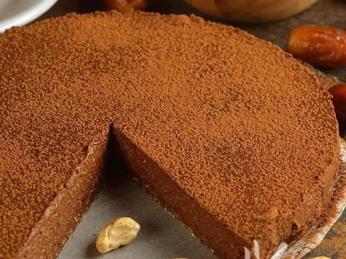 Deliziosa torta al cioccolato spolverata di cacao, con un anacardo in primo piano.
