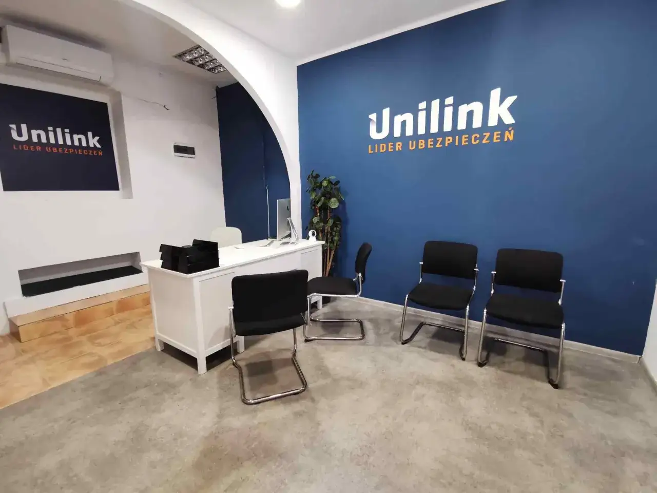 Biuro Unilink z logo firmy na niebieskiej ścianie, biurkiem i krzesłami.
