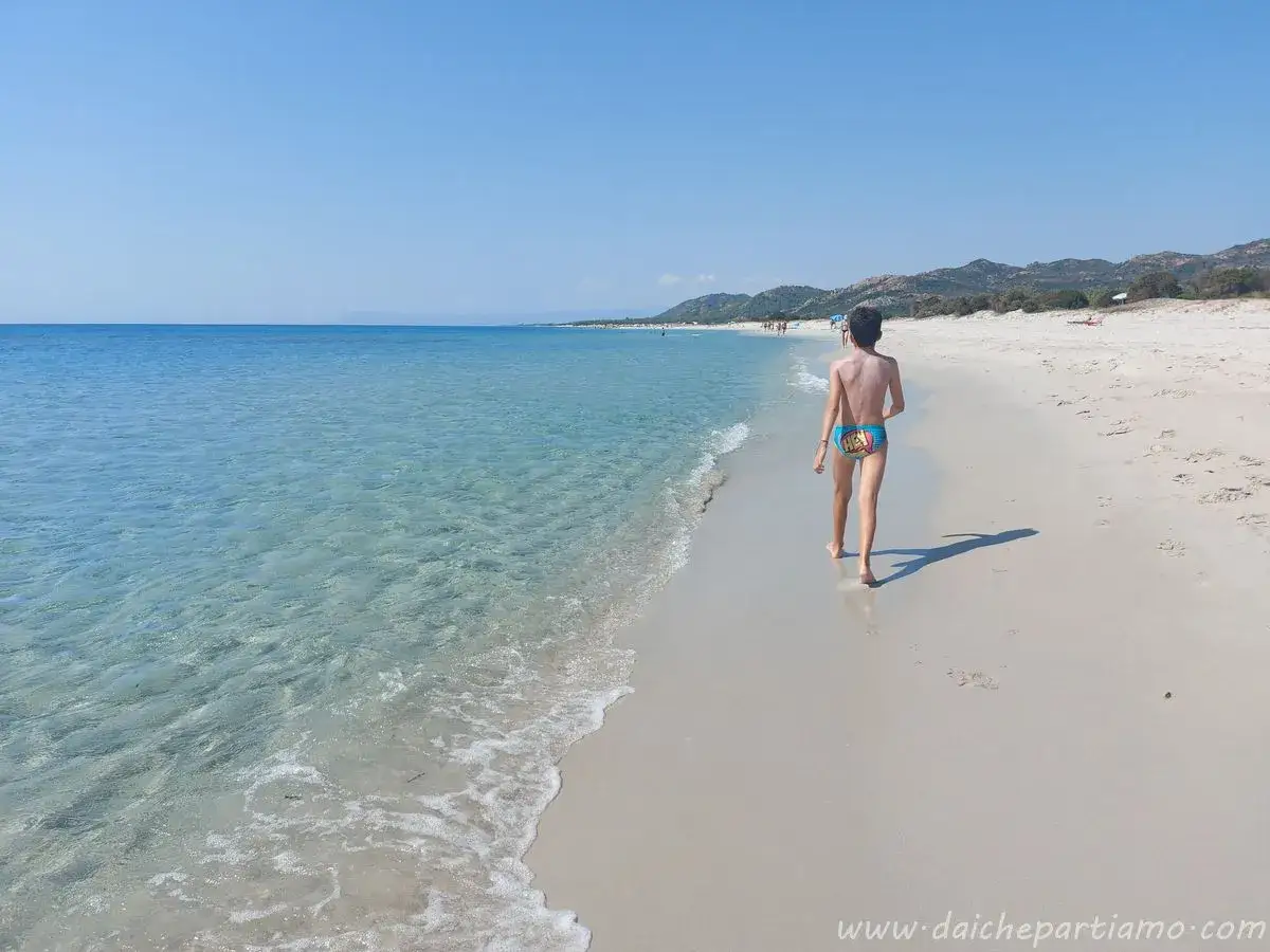 Bambino cammina sulla spiaggia della costa est Sardegna, mare cristallino e colline all'orizzonte.