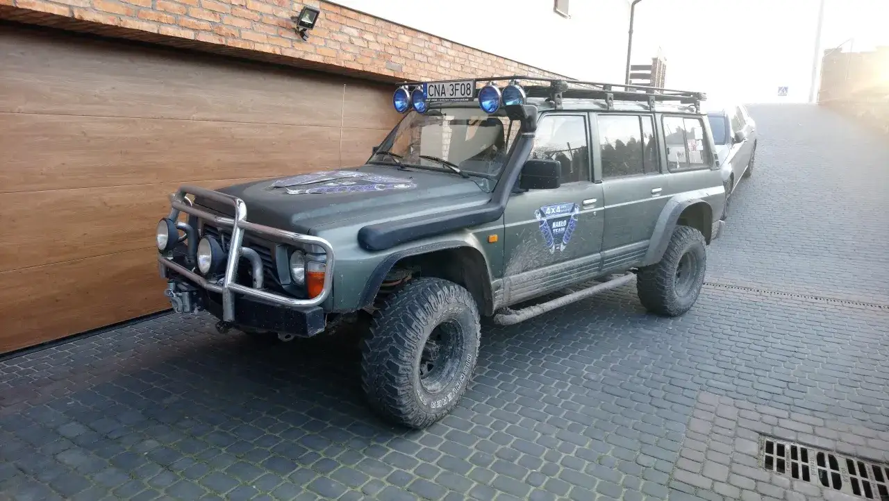 Zielony Nissan Patrol Y60 z bagażnikiem dachowym i wyciągarką, gotowy na terenową przygodę.