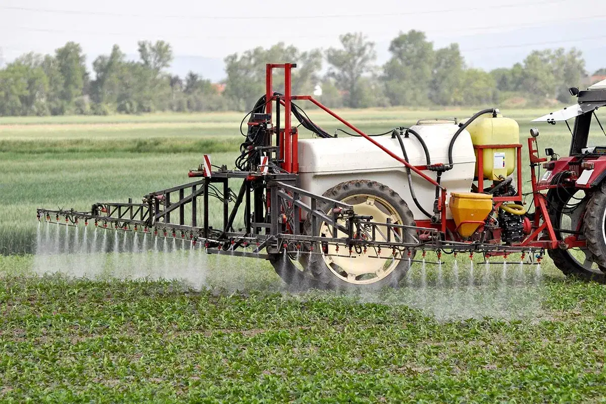 Traktor z opryskiwaczem, który rozpyla środek ochrony roślin, być może Afalon, na młode rośliny na polu.