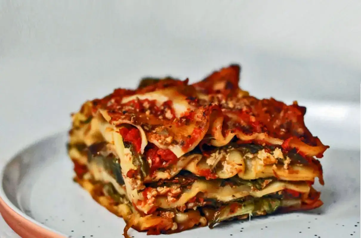 Pyszne lasagne z warzywami, z widocznymi warstwami makaronu, sosu pomidorowego i zielonych warzyw, podane na talerzu.