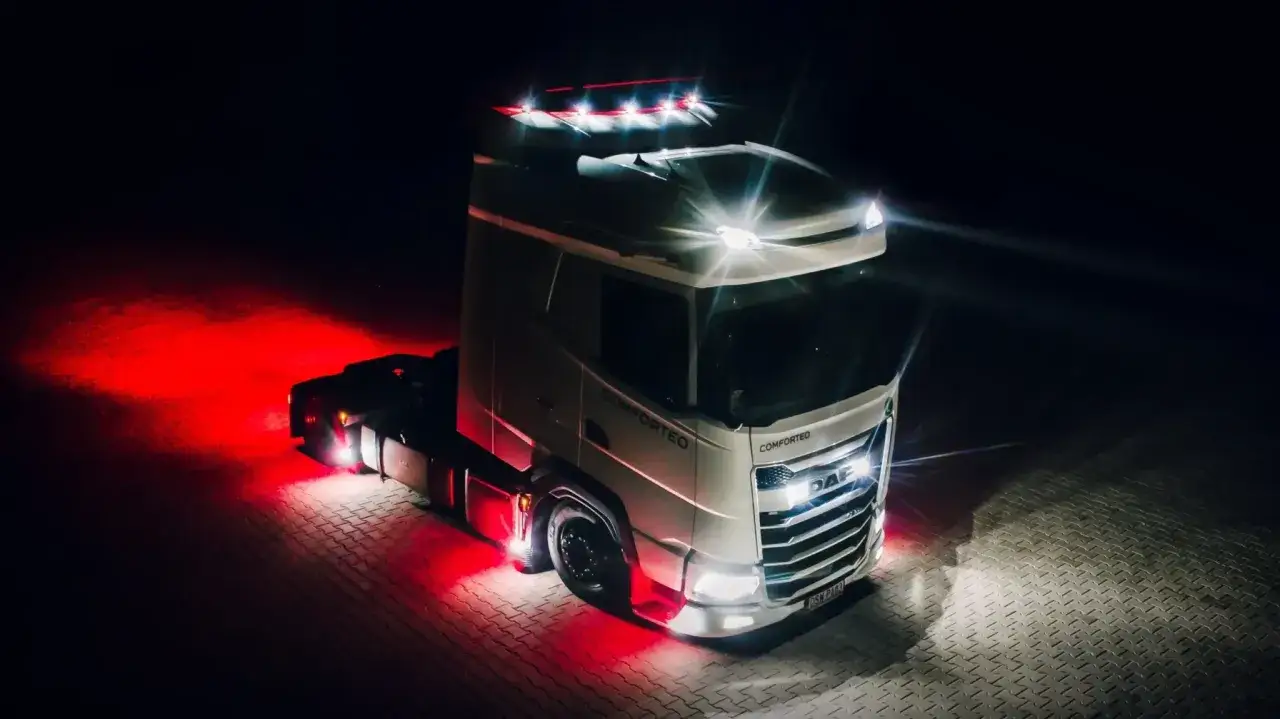 Camion DAF blanc la nuit, éclairé par des feux diurnes arrière rouges et des phares blancs éclatants.