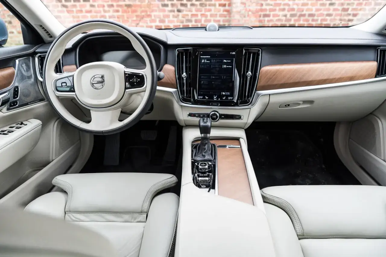 Luxuriöses Interieur eines Volvos mit hellem Leder und Holzverkleidung. Die Mittelkonsole zeigt den Gangwahlhebel und das Infotainmentsystem, das gute Volvo Geartronic Erfahrungen verspricht.