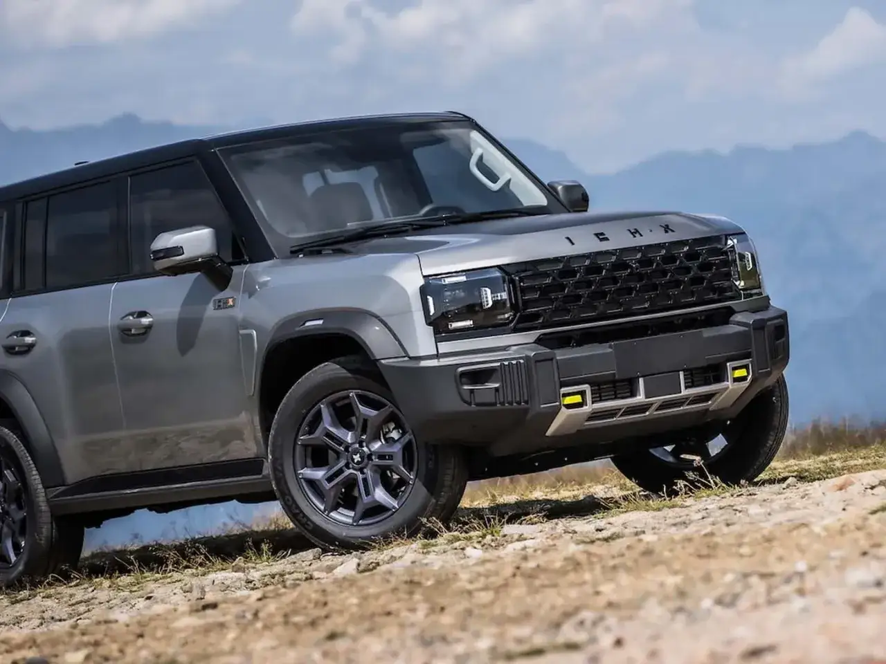 Un SUV grigio metallizzato, il ickx k3, affronta un terreno accidentato con montagne sullo sfondo.