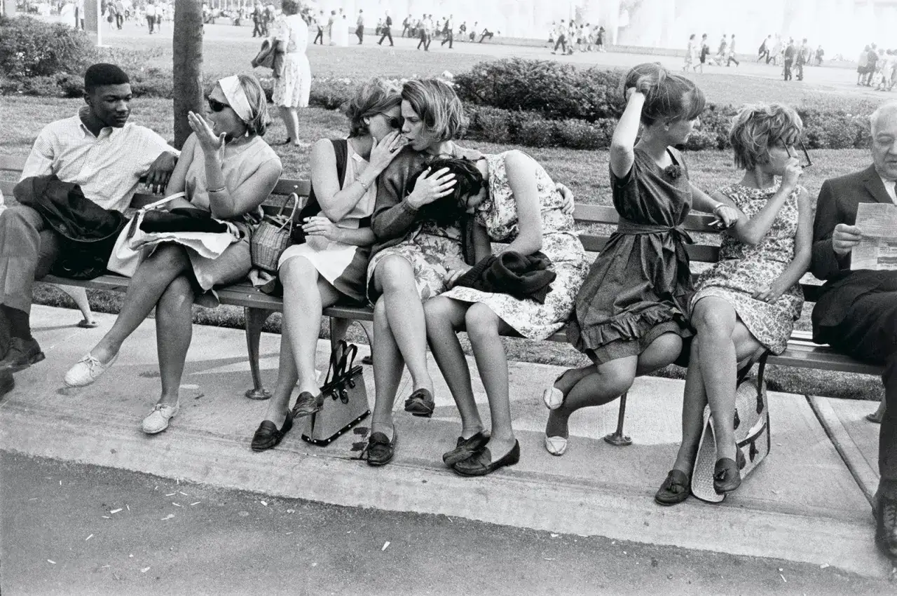 Garry Winogrand uchwycił grupę młodych ludzi na ławce. Dwie dziewczyny szepczą sobie do ucha, podczas gdy inne siedzą obok, wpatrzone w dal.