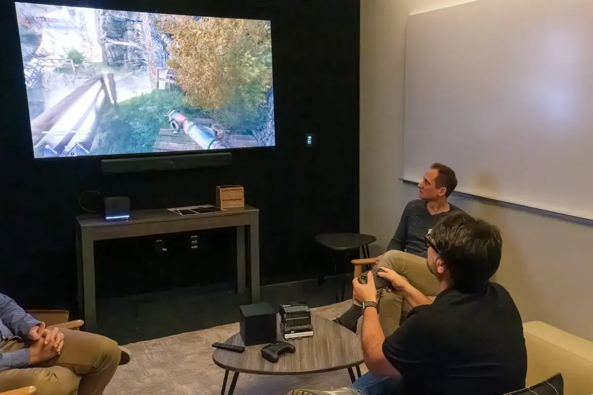 M&auml;nner spielen ein Spiel auf dem Bildschirm, das den **Steam Machine Release** feiert.