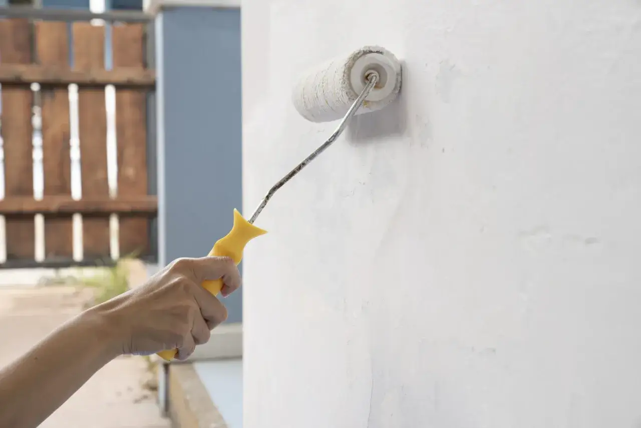 Mano aplica imprimación blanca con rodillo sobre pared texturizada. Se puede dar imprimación encima de pintura para un mejor acabado.