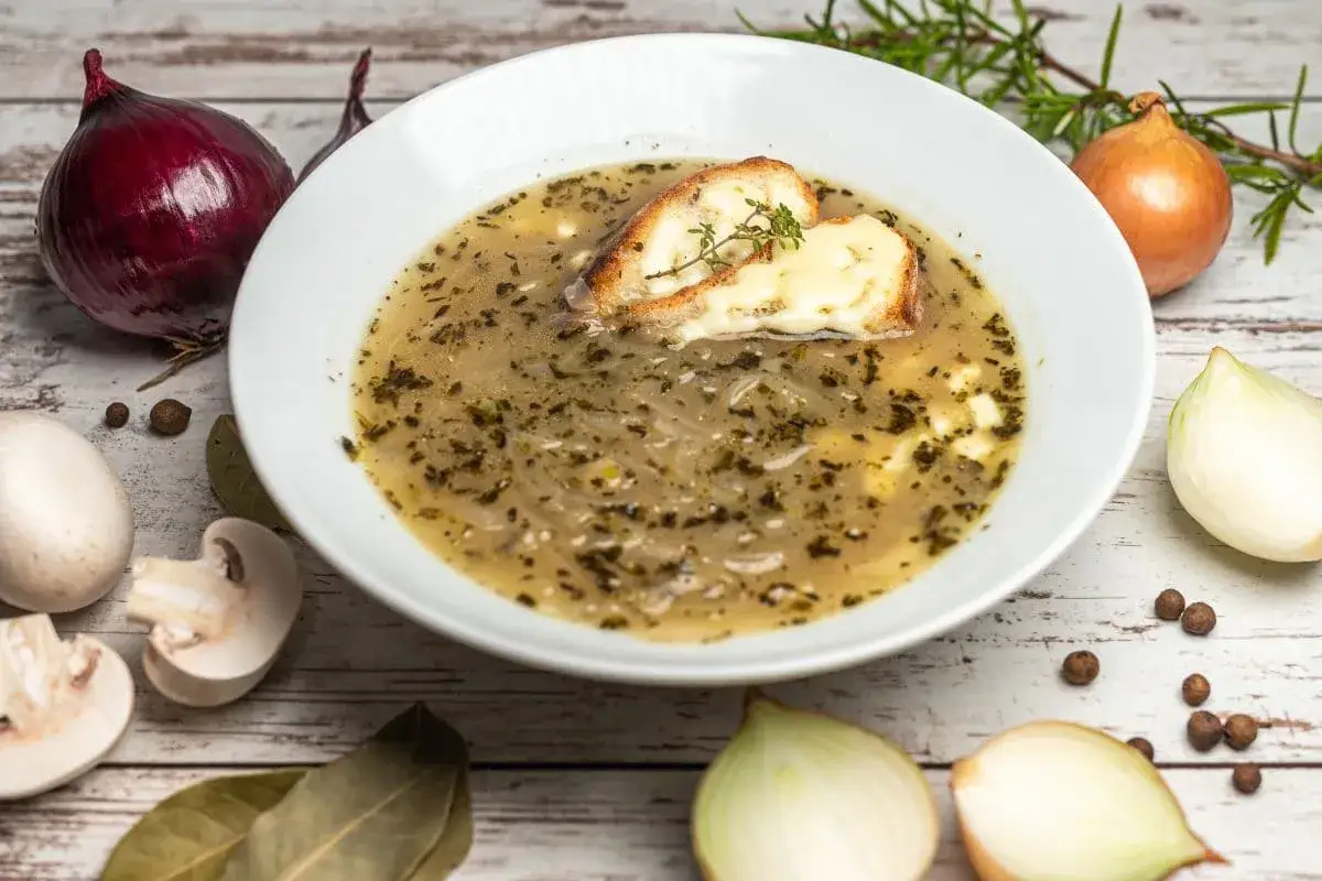 Pyszna zupa cebulowa przepis. Aromatyczna zupa z grzanką i serem, otoczona składnikami: cebulą, grzybami i przyprawami.