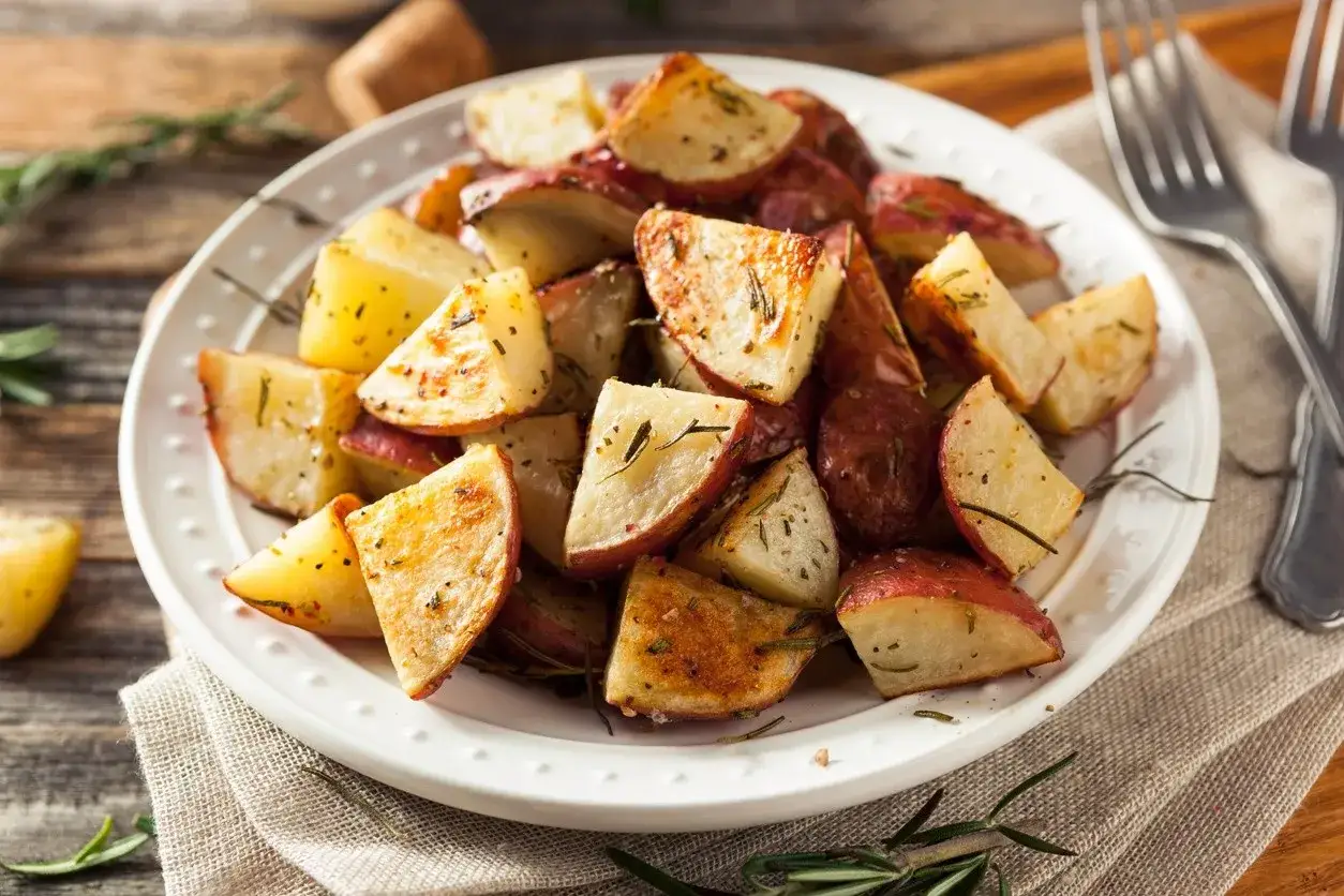 Patate al forno con buccia, dorate e profumate al rosmarino, servite su un piatto bianco.