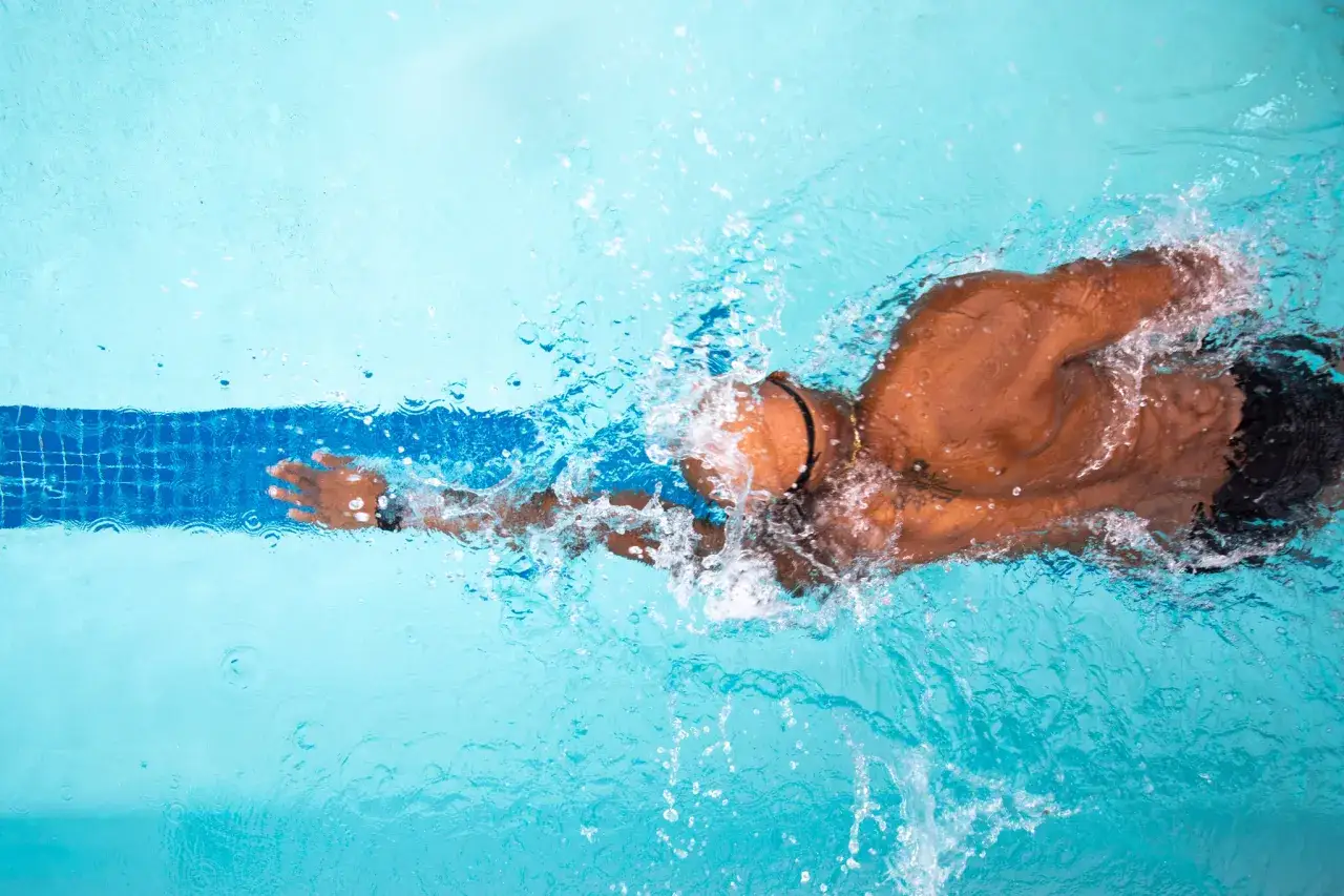 Un nageur effectue un exercice de natation en crawl, créant des éclaboussures d'eau bleues.