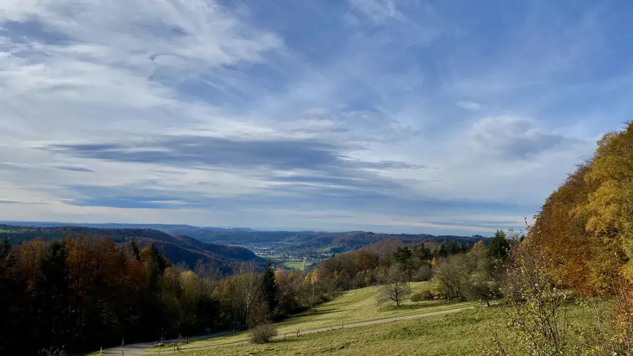 Herbstliche H&uuml;gellandschaft bei Welzheim, mit bunten B&auml;umen und einem Tal im Hintergrund. Die Wolken am Himmel scheinen wie feenspuren.