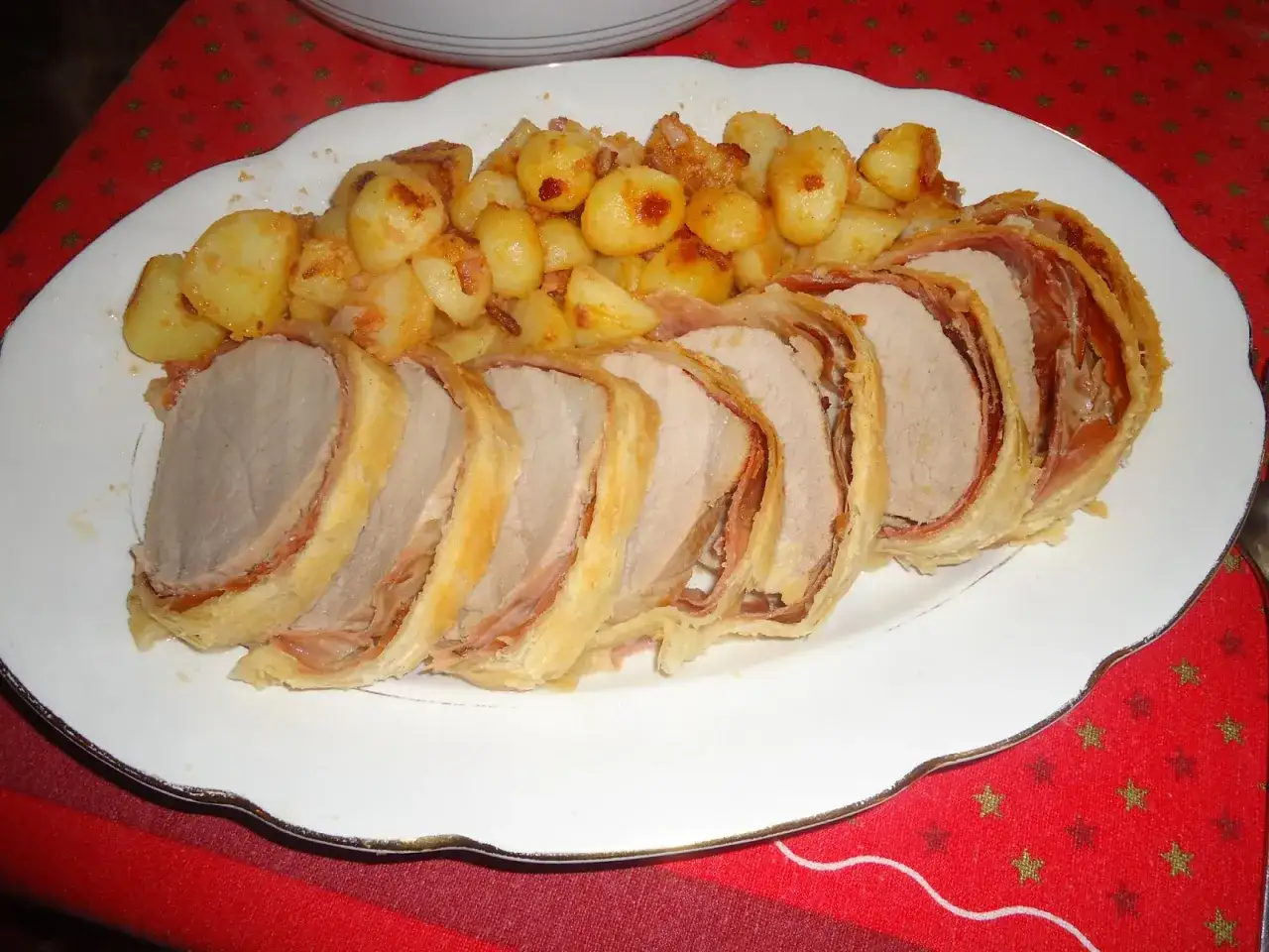 Delizioso arrosto di manzo avvolto in pasta sfoglia e prosciutto, servito con patate arrosto croccanti.
