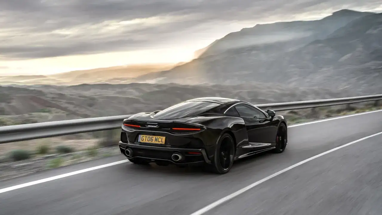 Czarny McLaren GT pędzi po krętej drodze w górach o zachodzie słońca.