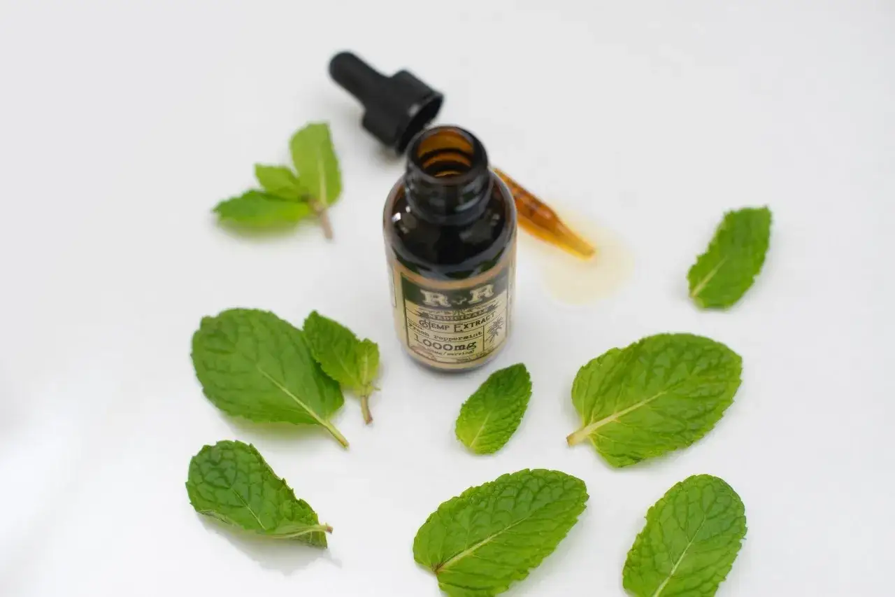 Flacon d'extrait de chanvre à la menthe poivrée, entouré de feuilles de menthe fraîche. Découvrez les menthe poivrée bienfaits.