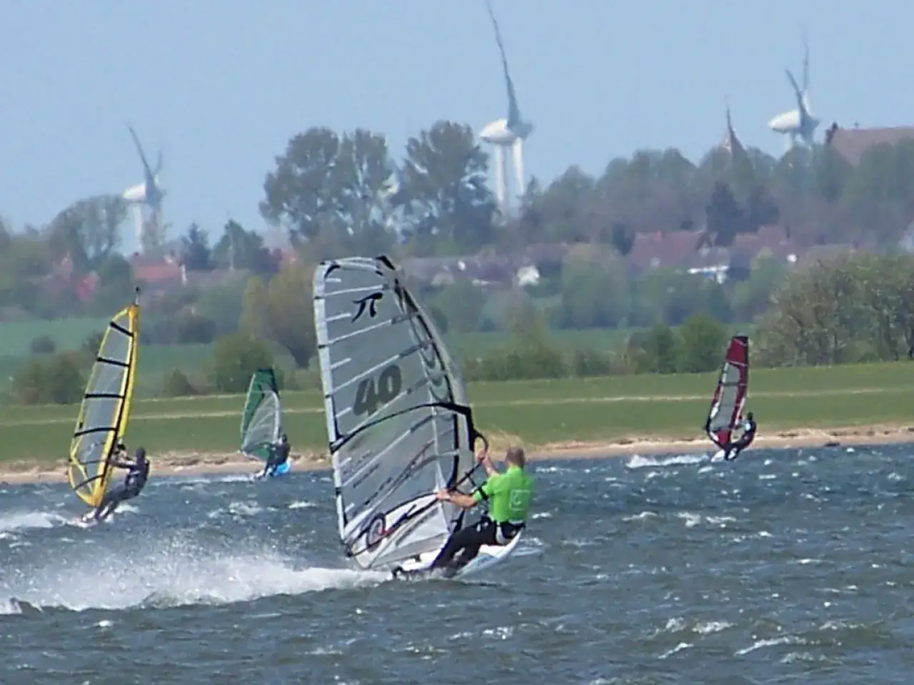 Windsurfer auf dem Wasser bei Wulfen, mit Windr&auml;dern im Hintergrund.