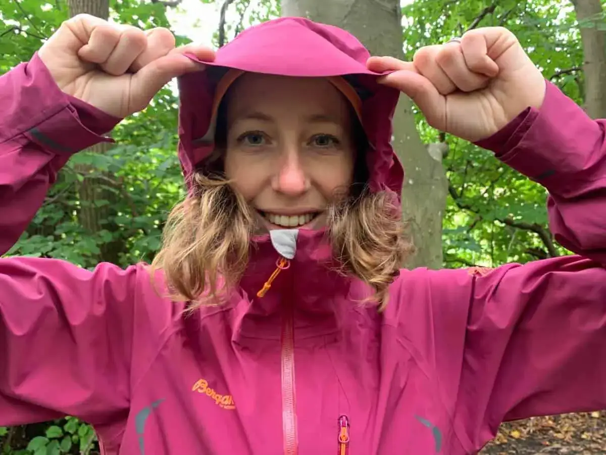 Kvinna i skogen drar upp huvan p&aring; sin rosa jacka. Den har en vattenpelare p&aring; 10000, perfekt f&ouml;r svenskt v&auml;der.