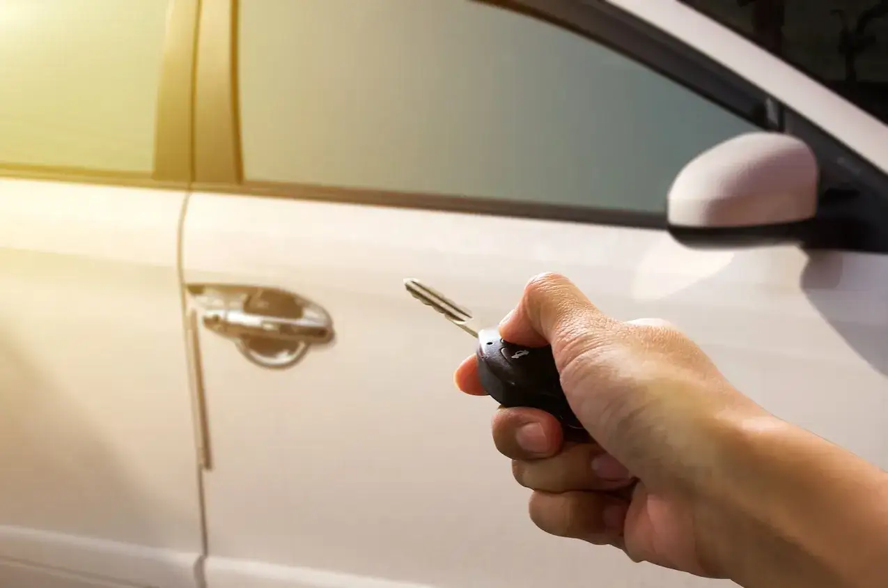 Mano sujetando llave para resetear cierre centralizado de un coche blanco.
